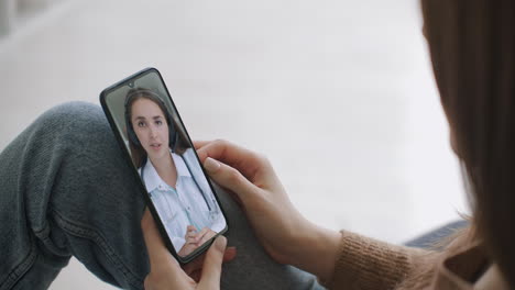 Woman-checks-possible-symptoms-with-professional-physician-using-online-video-chat.-Young-girl-sick-at-home-using-smartphone-to-talk-to-her-doctor-via-video-conference-medical-app.